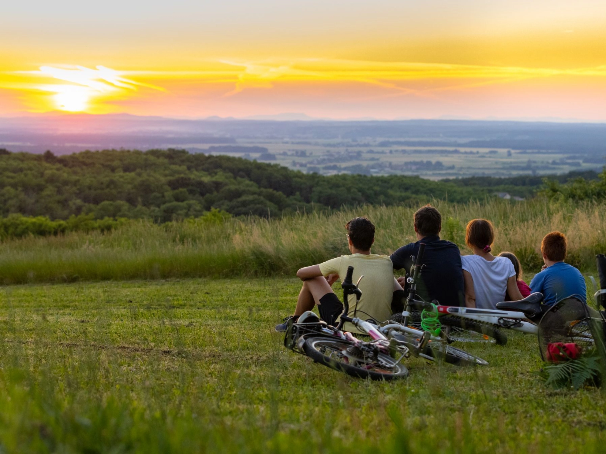 Familie, die nach einer Radtour auf einem Hügel sitzt und den Sonnenuntergang betrachtet 