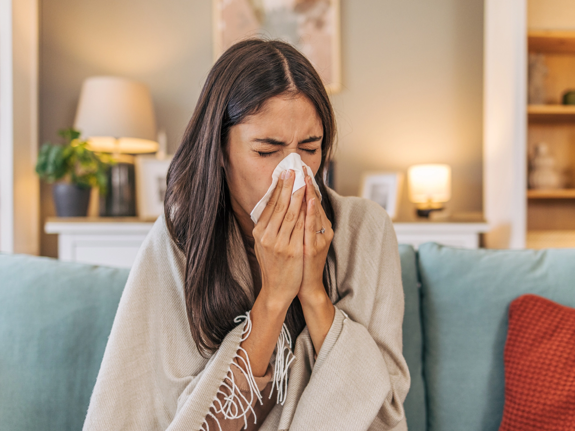 Eine erkältete Frau sitzt auf einem Sofa und putzt sich die Nase.